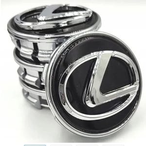 May include: A stack of four circular wheel center caps featuring a glossy black background and a raised, polished chrome Lexus logo. Each cap has a metallic silver outer ring and a series of plastic clips on the underside for secure attachment.