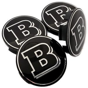 Peut inclure: Ensemble de cinq enjoliveurs de roue noirs et argentés. Chaque enjoliveur présente un grand "B" blanc stylisé dans un bord argenté sur un fond noir brillant. Les enjoliveurs sont ronds et ont une apparence tridimensionnelle.