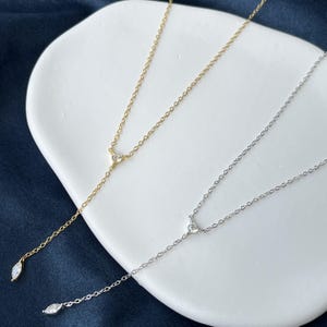 May include: Two delicate lariat necklaces, one in gold tone and one in silver tone, each featuring a small round stone at the centre junction and a single marquise-cut stone dangling at the end of the vertical chain segment.