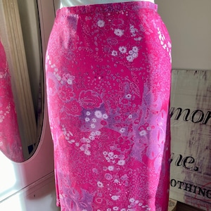 Puede incluir: Una falda rosa con estampado floral. La falda tiene un estampado floral blanco y morado sobre un fondo rosa.