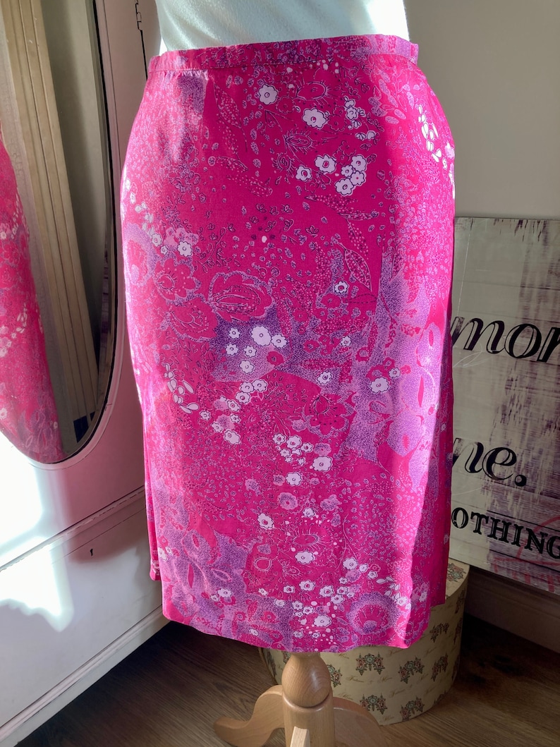 Puede incluir: Una falda rosa con estampado floral. La falda tiene un estampado floral blanco y morado sobre un fondo rosa.