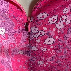 Puede incluir: Primer plano de una tela de estampado floral rosa y morado con una cremallera que baja por el centro.