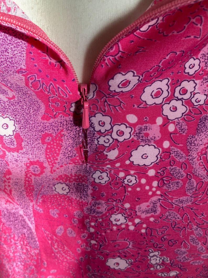 Puede incluir: Primer plano de una tela de estampado floral rosa y morado con una cremallera que baja por el centro.