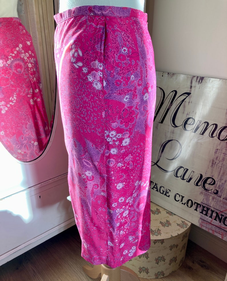 Puede incluir: Una falda rosa con estampado floral en tonos morados y blancos. La falda es de largo hasta la rodilla y tiene una silueta recta.