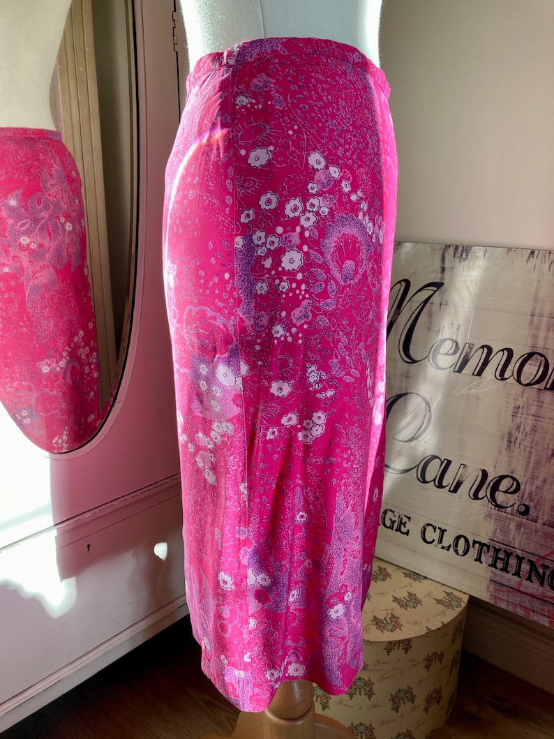 Puede incluir: Una falda rosa con estampado floral. La falda tiene un fondo blanco con flores rosas y moradas.