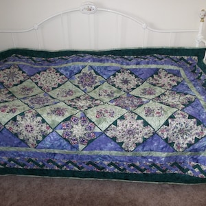 May include: A green, purple, and blue patchwork quilt with a floral pattern. The quilt is on a white metal bed frame.