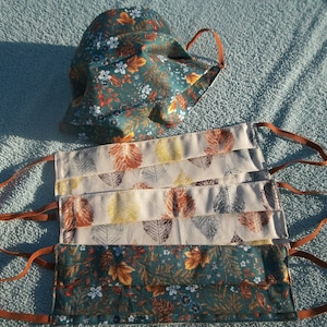 May include: Four face masks with autumn-themed fabric patterns. The masks are made of a soft, breathable material and have adjustable ear loops. The patterns include leaves, pine cones, and flowers in shades of brown, orange, yellow, and green.