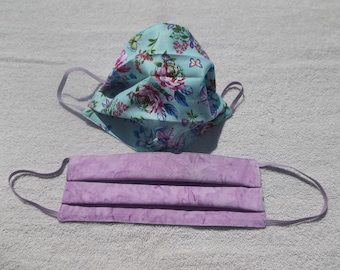 May include: Two face masks, one with a floral pattern on a light blue background and the other a solid light purple color.