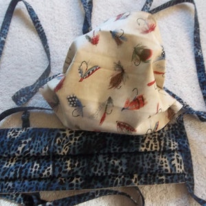 May include: Two face masks with ties. One mask is white with a pattern of colorful fishing flies. The other mask is blue with a leopard print pattern.