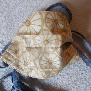 May include: A beige face mask with a white and brown floral pattern. The mask has blue ties.