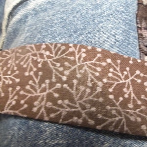 K&ouml;nnte beinhalten: Ein braunes Stoffband mit einem wei&szlig;en Blumenmuster. Das Band ist an einer blauen Jeans befestigt.