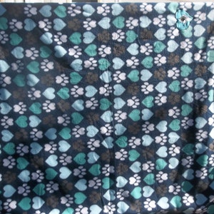 May include: A blue fleece blanket with a pattern of white hearts and teal paw prints. The blanket has a knotted fringe on all sides.