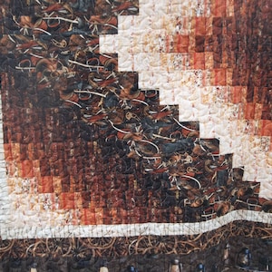 May include: A quilt with a brown, white, and orange patchwork design. The quilt is made of squares of fabric sewn together in a diagonal pattern. The quilt is edged with a white trim.