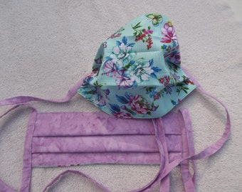 May include: Two face masks, one with a floral pattern on a light blue background and the other with a purple tie-dye pattern. Both masks have matching purple ties.