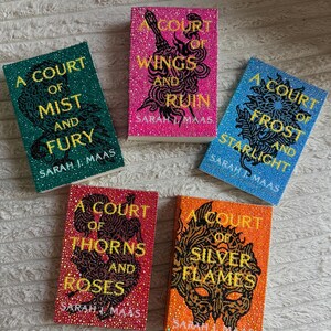 May include: Five books with embellished covers. The titles include "A Court of Mist and Fury", "A Court of Wings and Ruin", "A Court of Frost and Starlight", "A Court of Thorns and Roses", and "A Court of Silver Flames". Each book has a different colour scheme.