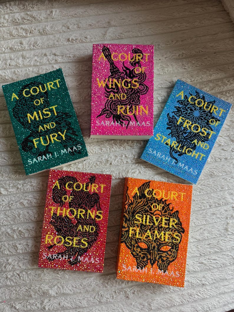 May include: Five books with embellished covers. The titles include "A Court of Mist and Fury", "A Court of Wings and Ruin", "A Court of Frost and Starlight", "A Court of Thorns and Roses", and "A Court of Silver Flames". Each book has a different colour scheme.