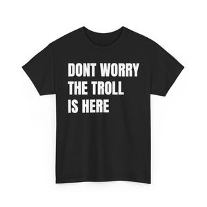 Pode incluir: Uma t-shirt preta de manga curta com o texto branco DONT WORRY THE TROLL IS HERE impresso numa fonte sem serifa em negrito no peito. A peça tem um decote redondo clássico e uma bainha reta, proporcionando um design simples e limpo.