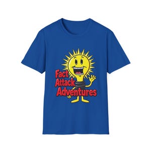 Pode incluir: Uma t-shirt de manga curta azul-real com um gráfico de uma lâmpada amarela com um sorriso largo e raios pontiagudos. O texto "Fact Attack Adventures" está impresso em letras vermelhas a negrito à esquerda da personagem lâmpada.