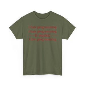 K&ouml;nnte beinhalten: Ein olivgr&uuml;nes Kurzarm-T-Shirt mit rotem Textaufdruck: I hate programming, I hate programming, &mdash; It works! &mdash;, I love programming. Das Shirt hat einen Rundhalsausschnitt und eine normale Passform, wobei der Text mittig auf der Brust platziert ist.