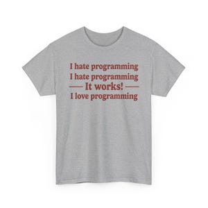 K&ouml;nnte beinhalten: Ein graumeliertes Kurzarm-T-Shirt mit dunkelrotem Textaufdruck auf der Vorderseite. Der Text lautet: I hate programming, I hate programming, &mdash; It works! &mdash;, I love programming. Das T-Shirt hat einen Rundhalsausschnitt und eine Standardpassform.