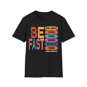 Op de afbeelding: Een zwart t-shirt met korte mouwen en de tekst BE FAST in grote, verweerde, veelkleurige letters. Rechts staan zes horizontale gekleurde balken met de woorden BALANCE, EYES, FACE, ARMS, SPEECH, TIME en daaronder #Stroke Awareness.