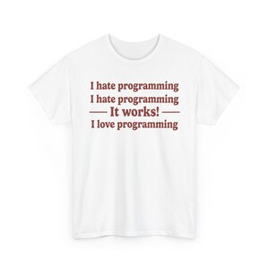 Pode incluir: Uma t-shirt branca de manga curta com texto vermelho escuro centrado no peito que diz: I hate programming, I hate programming, It works!, I love programming. A t-shirt tem um decote redondo e um corte padrão com mangas curtas.