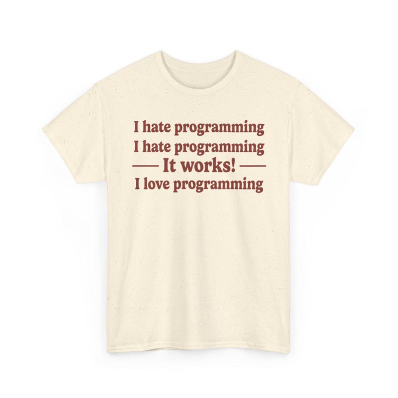 K&ouml;nnte beinhalten: Ein cremefarbenes Kurzarm-T-Shirt mit gesprenkelter Textur. Auf der Vorderseite befindet sich ein dunkelbrauner Text: I hate programming, I hate programming, &mdash; It works! &mdash;, I love programming. Das T-Shirt hat einen Rundhalsausschnitt und einen geraden Saum.