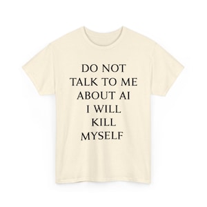 Pode incluir: Uma t-shirt de manga curta na cor creme com uma textura salpicada. A parte frontal apresenta um texto preto que diz: DO NOT TALK TO ME ABOUT AI I WILL KILL MYSELF. A peça tem um decote redondo e um corte padrão em tecido de cor clara.