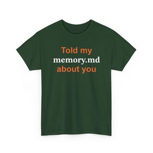 Puede incluir: Una camiseta de manga corta de color verde bosque oscuro con el texto "Told my memory.md about you" impreso en el pecho. Las palabras "Told my" y "about you" son de color naranja, mientras que "memory.md" es blanca, centrada en una fuente serif.