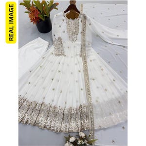 May include: A white long-sleeved floor-length dress featuring silver embroidery and mirror work on the bodice, cuffs, and hem. The dress includes a matching white dupatta with scattered silver embellishments and a pair of white trousers.