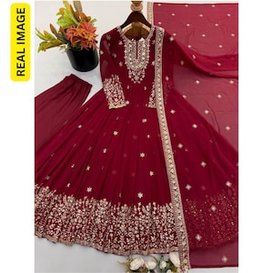 May include: A deep maroon long-sleeved floor-length dress featuring intricate gold embroidery around the neckline, cuffs, and hem. The dress includes a matching maroon dupatta with small gold accents and plain maroon trousers, all displayed on a hanger.
