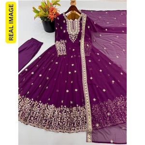 May include: A deep purple floor-length gown featuring intricate gold embroidery around the neckline, cuffs, and hem. The dress includes a matching sheer dupatta with gold accents and solid purple trousers, showcasing a floral and geometric pattern.