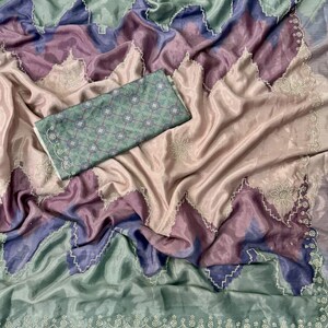 May include: A draped, silky fabric in shades of pink, purple, and blue, with a green border and a matching patterned piece. The fabric has a shimmering quality, with a scalloped edge and delicate white beadwork.