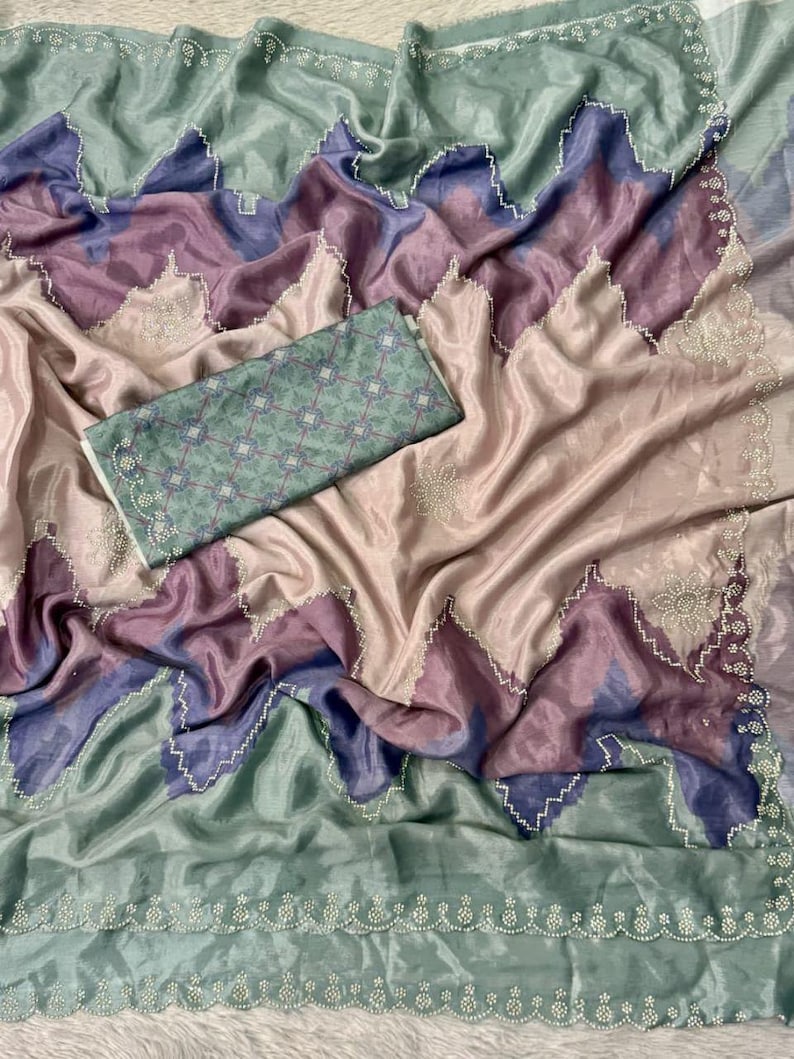 May include: A draped, silky fabric in shades of pink, purple, and blue, with a green border and a matching patterned piece. The fabric has a shimmering quality, with a scalloped edge and delicate white beadwork.