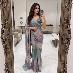 May include: A woman in a mirror selfie wearing a flowing saree. The saree features a patchwork design in shades of green, purple, and pink. The top is a darker green with a V-neck. The mirror has an ornate gold frame.