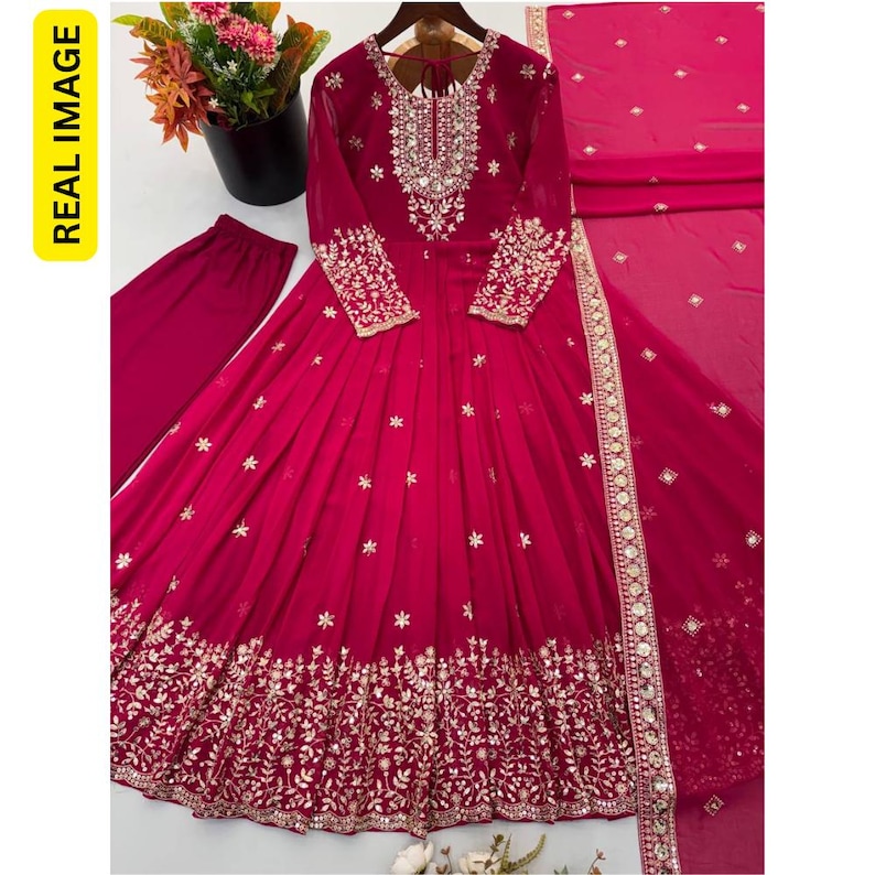May include: A magenta long-sleeved floor-length dress featuring intricate silver embroidery around the neckline, cuffs, and hem. The dress includes a matching magenta pair of trousers and a coordinating magenta dupatta with silver floral accents.