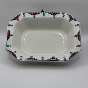 Puede incluir: Una fuente rectangular de cerámica blanca con un borde floral decorativo. El borde presenta diseños florales rojos y azules con detalles verdes. La fuente tiene un borde ligeramente elevado y un acabado brillante.