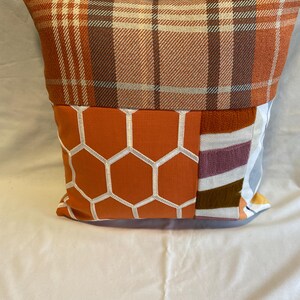 May include: A decorative throw pillow with a patchwork design featuring orange, brown, white, and gray plaid, honeycomb, and striped patterns.