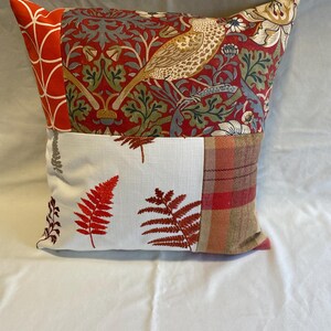 May include: A patchwork cushion with a red, white and brown colour scheme. The cushion features a bird, floral and fern patterns.