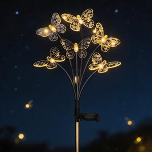 Pode incluir: Uma estaca de jardim movida a energia solar com seis decorações de borboletas iluminadas. As borboletas têm intrincados desenhos de asas e emitem um brilho amarelo quente. A estaca é preta e dourada, contra um céu noturno azul escuro com luzes suaves e desfocadas.
