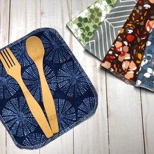 Puede incluir: Una servilleta de tela azul marino con un estampado floral blanco, un tenedor de madera y una cuchara de madera. Tambi&eacute;n se ven varias servilletas estampadas en verde, gris, marr&oacute;n y azul. Las servilletas son de tela suave.