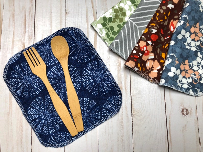 Puede incluir: Una servilleta de tela azul marino con un estampado floral blanco, un tenedor de madera y una cuchara de madera. Tambi&eacute;n se ven varias servilletas estampadas en verde, gris, marr&oacute;n y azul. Las servilletas son de tela suave.