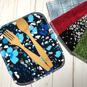 Puede incluir: Un pa&ntilde;o cuadrado negro con un estampado floral azul, un tenedor de madera y una cuchara de madera. Se ven varios otros pa&ntilde;os estampados, incluyendo un pa&ntilde;o gris con puntos blancos, un pa&ntilde;o rojo con un estampado de hojas, un pa&ntilde;o negro con flores blancas y un pa&ntilde;o verde con peque&ntilde;os puntos.