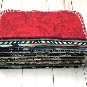 Puede incluir: Una pila de servilletas de tela con varios patrones y colores. La servilleta superior es roja con un dise&ntilde;o de hojas y costuras blancas. Otras servilletas presentan rayas, dise&ntilde;os florales y abstractos. Las servilletas est&aacute;n cuidadosamente apiladas, mostrando una variedad de dise&ntilde;os de tela.