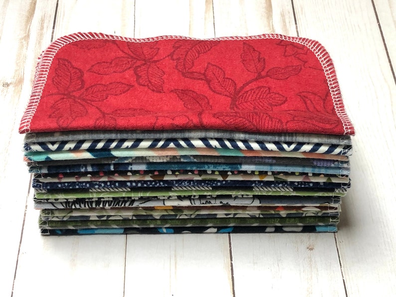 Puede incluir: Una pila de servilletas de tela con varios patrones y colores. La servilleta superior es roja con un dise&ntilde;o de hojas y costuras blancas. Otras servilletas presentan rayas, dise&ntilde;os florales y abstractos. Las servilletas est&aacute;n cuidadosamente apiladas, mostrando una variedad de dise&ntilde;os de tela.