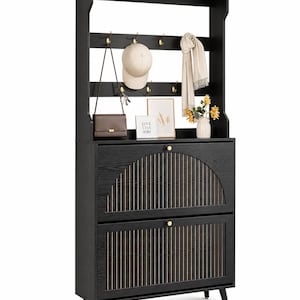 Könnte beinhalten: Ein schwarzes Eingangsspeichergerät mit eingebautem Kleiderständer. Das Gerät verfügt über zwei Schubladen mit goldfarbenen Griffen und ein dekoratives vertikales Holzdesign. Eine Handtasche, eine Mütze und ein Schal hängen an der Stange. Ein kleines gerahmtes Bild und eine Vase mit Blumen befinden sich oben.