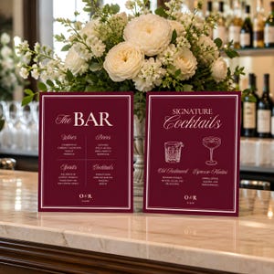 May include: Two rectangular burgundy signs with white text and borders. The left sign reads The BAR with lists for Wines, Beers, Spirits, and Cocktails. The right sign reads SIGNATURE Cocktails with illustrations of an Old Fashioned and Espresso Martini.