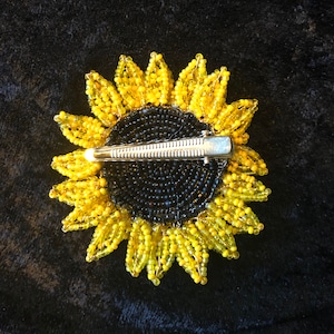 May include: A beaded sunflower hair clip with a black center and yellow petals. The clip is made of metal and has a spring-loaded mechanism.