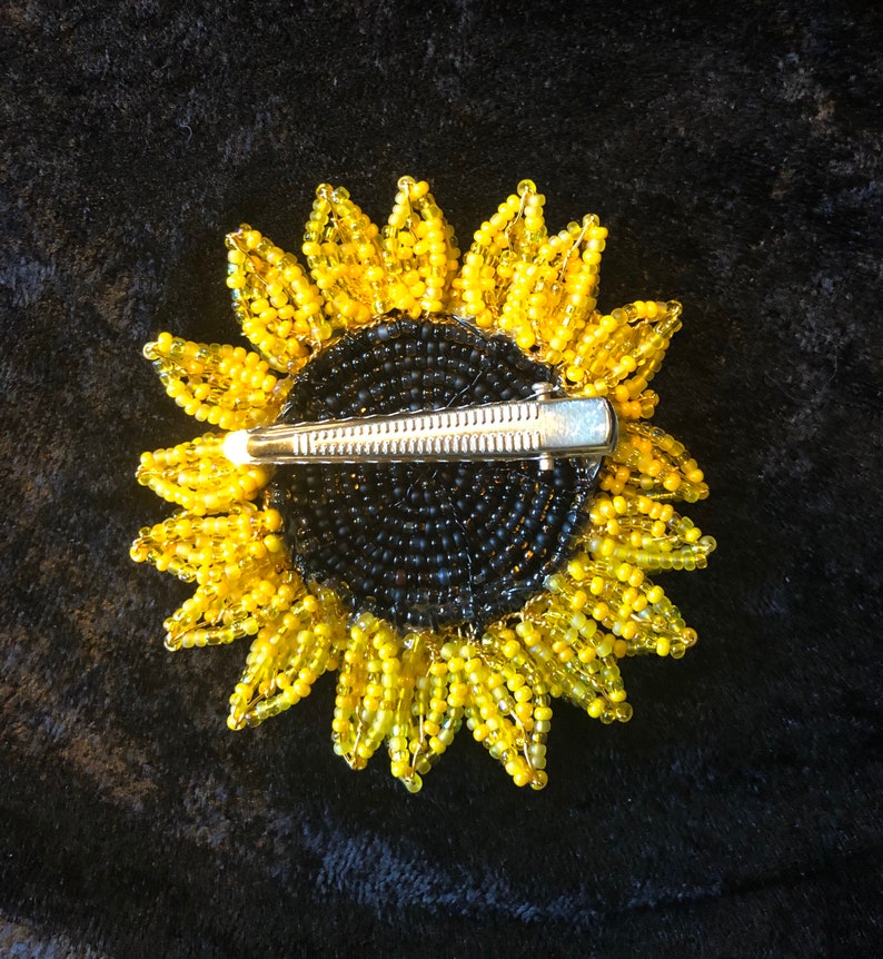 May include: A beaded sunflower hair clip with a black center and yellow petals. The clip is made of metal and has a spring-loaded mechanism.