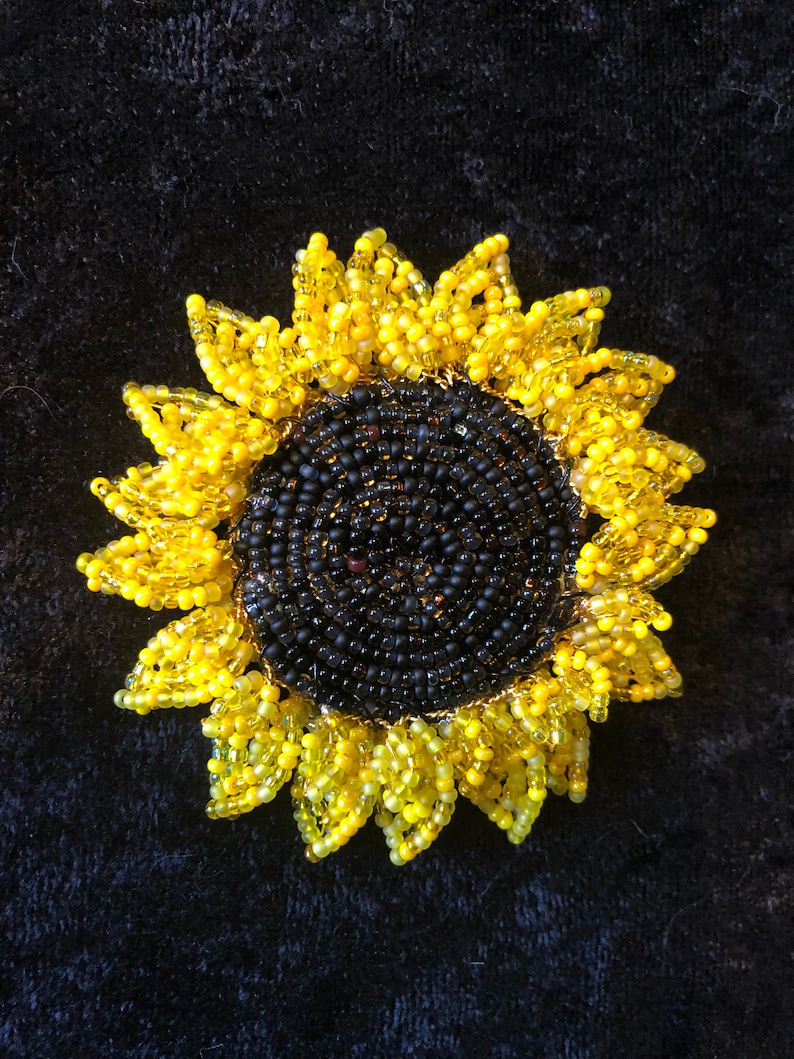 May include: A beaded sunflower brooch with a black center and yellow petals. The sunflower is made of small, round beads.